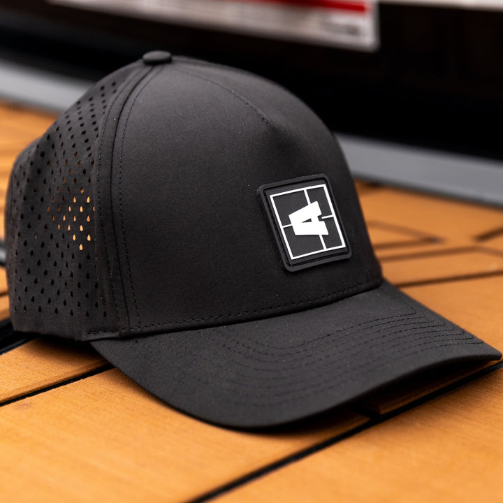 Black Axis Swell Hat with perforated panels and a rectangular logo patch on the front, placed on a wooden surface.