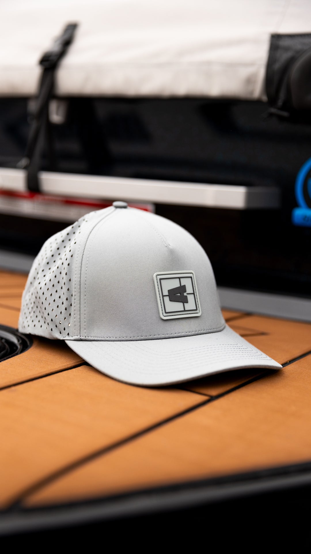 White Axis Swell Hat with a rectangular logo patch, perforated side panels, and curved brim, placed on a wooden surface.