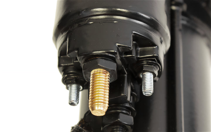 Close-up of black starter motor with small and big block bolts, showing metallic threaded studs on a vehicle engine part.