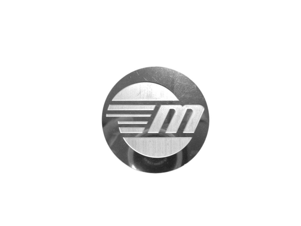 Gussi 931 steering wheel Malibu logo emblem, round metallic badge with stylized "M" and horizontal lines.