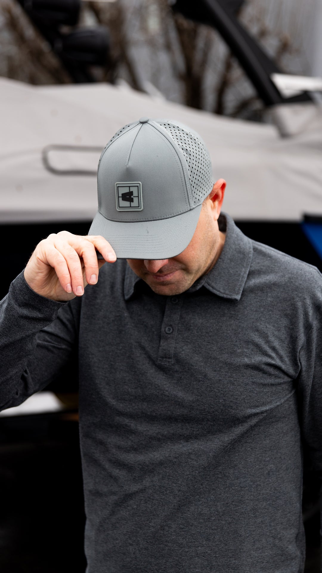 Man wearing a light gray Axis Swell Hat with perforated panels, adjusting the brim outdoors.