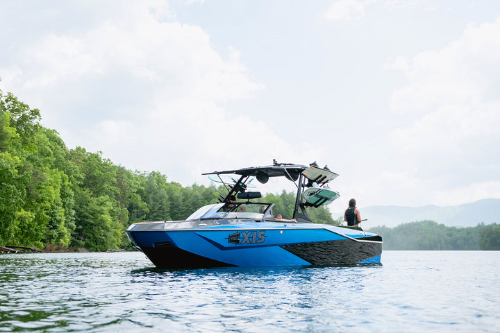 Blue Axis AW20 Bimini Boot on a lake with green trees, featuring a black canopy and multiple mounted wakeboards.