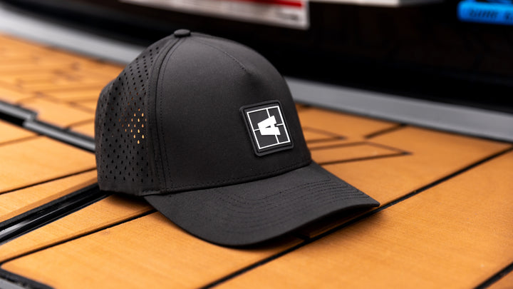 Black Axis Swell Hat with perforated side panels and a rectangular logo patch on the front, placed on a wooden surface.