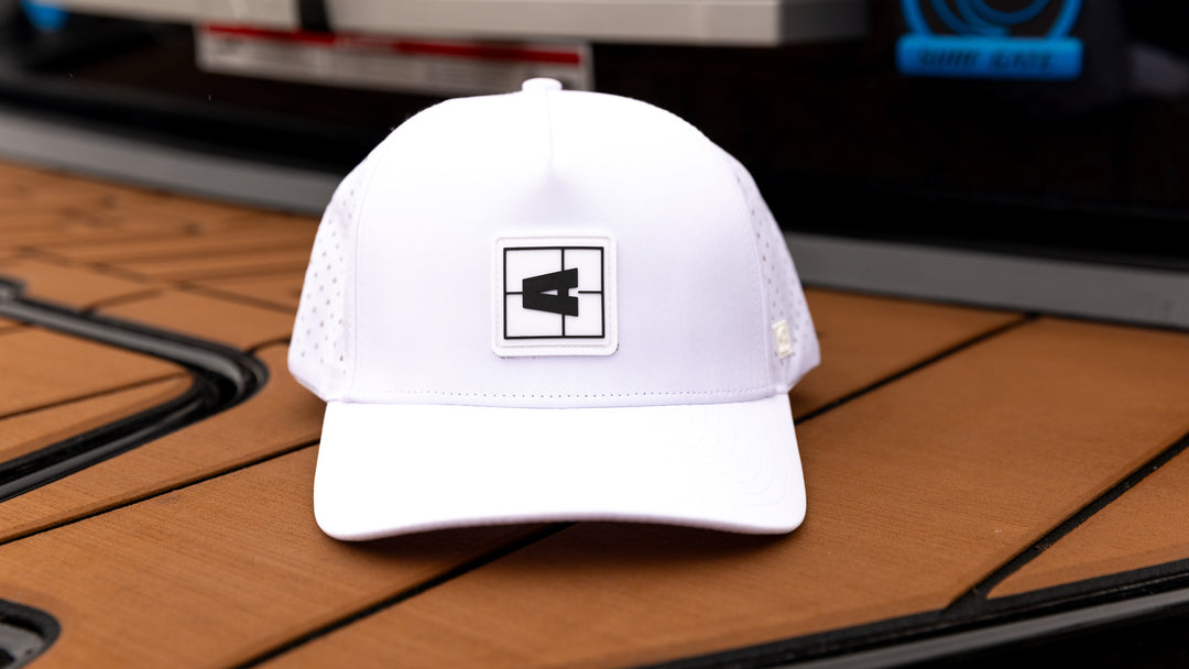 White Axis Swell Hat with a black and white logo patch, mesh panels on sides, and curved brim, displayed on a wooden surface.