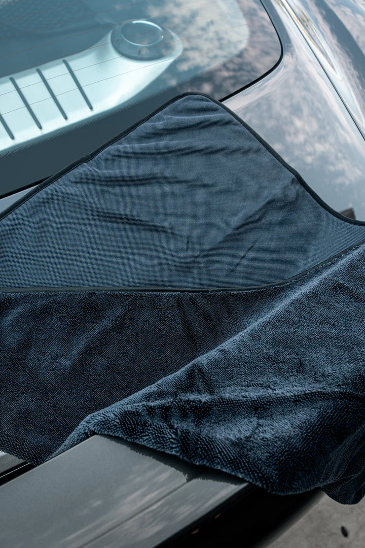 Slim twisted-loop drying towel draped over a car hood, showcasing its absorbent texture and sleek design for effective drying.