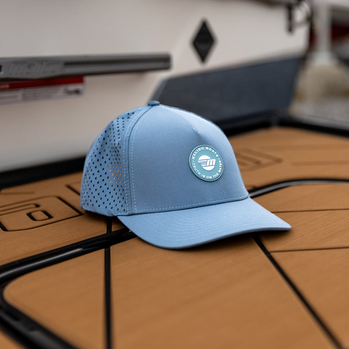 Light blue Malibu Truth Hat with perforated panels, circular logo patch, and curved brim, placed on a wooden surface.