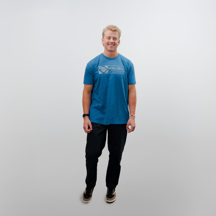 A person wearing a blue Malibu Icon Tee stands against a plain background, showcasing the shirt&