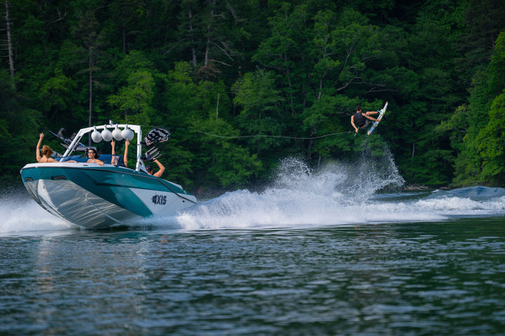 Axis AW20 Tower in white, showcasing a boat with riders enjoying water sports on a scenic lake surrounded by greenery.