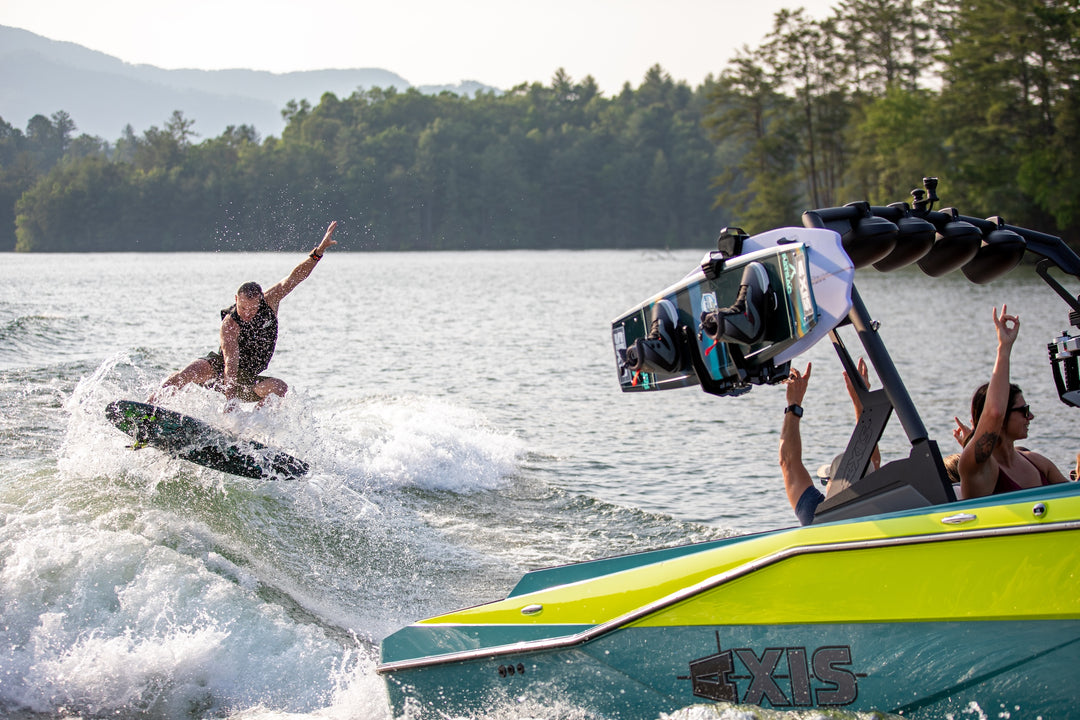 Axis AW20 Tower in black, showcasing a wakeboarder riding a wave with a vibrant boat in the foreground.
