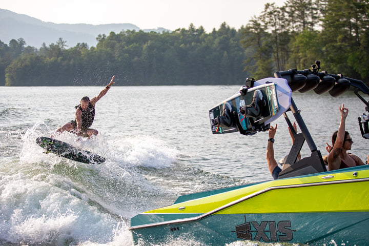 Axis AW20 Tower in black, showcasing a wakeboarder riding a wave with a vibrant boat in the foreground.