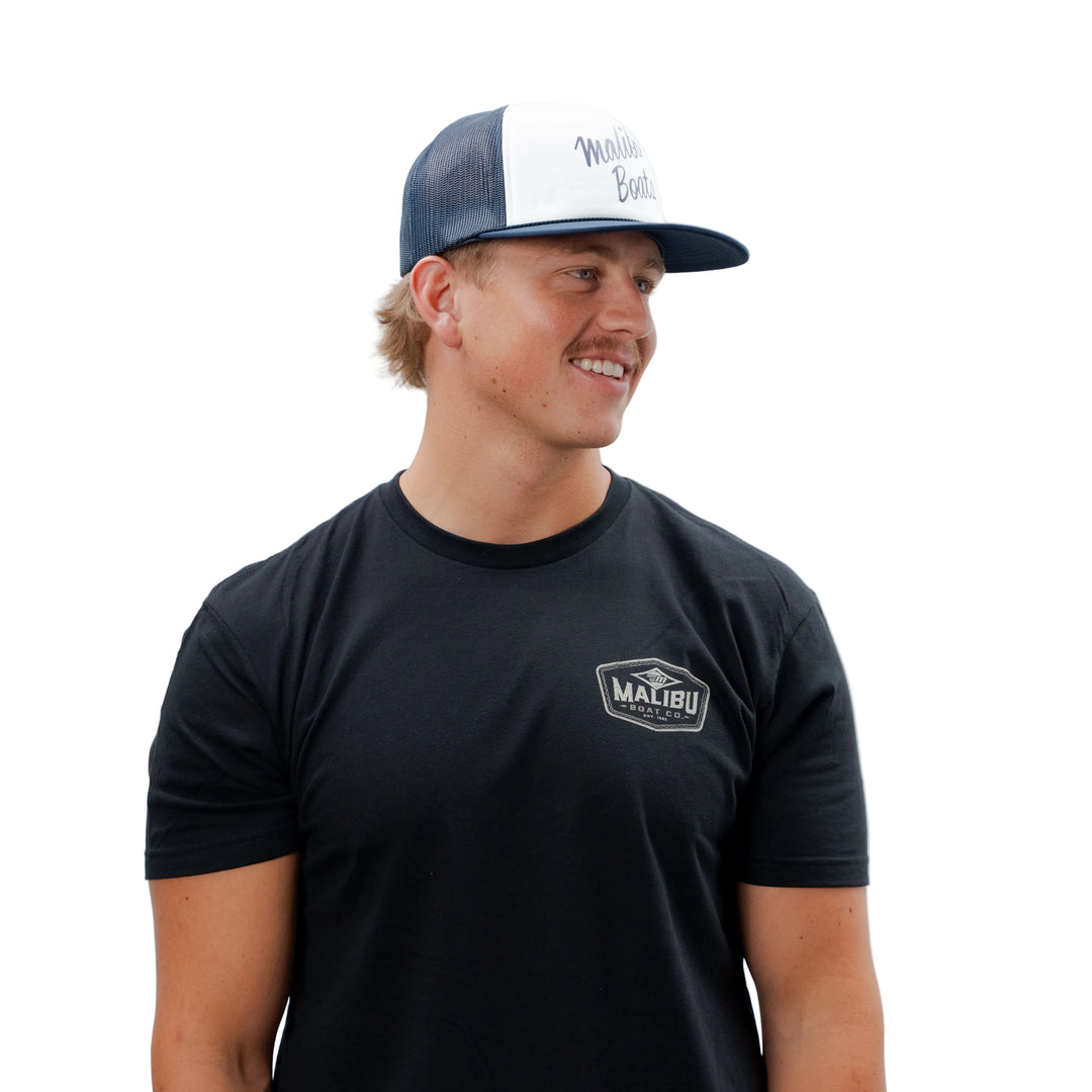 Young man wearing a black Malibu Boat Co. T-shirt and a navy and white trucker cap with "Malibu Diamond" text, smiling sideways.