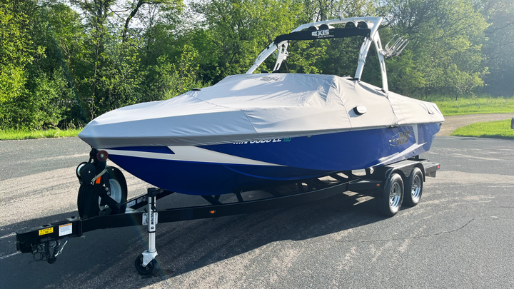 Aluminum boat with T22 Cover on a trailer, parked on a paved surface with green trees in the background.