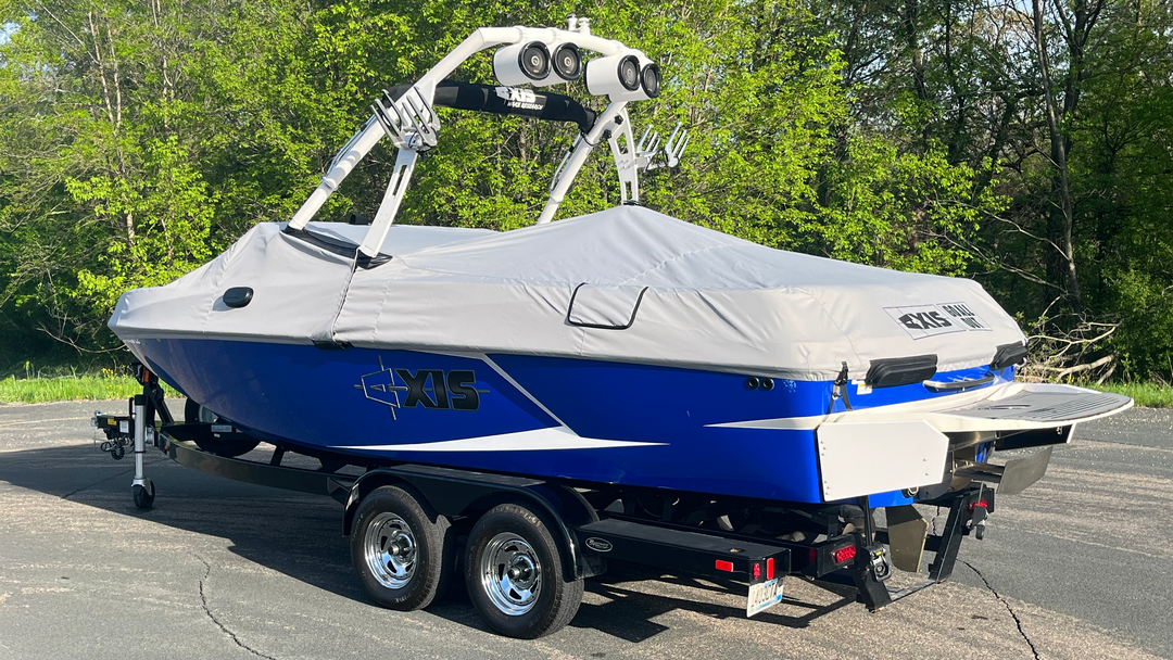 Blue and white T22 Cover for FatAX Tower boat on a trailer, parked on asphalt with green trees in the background.