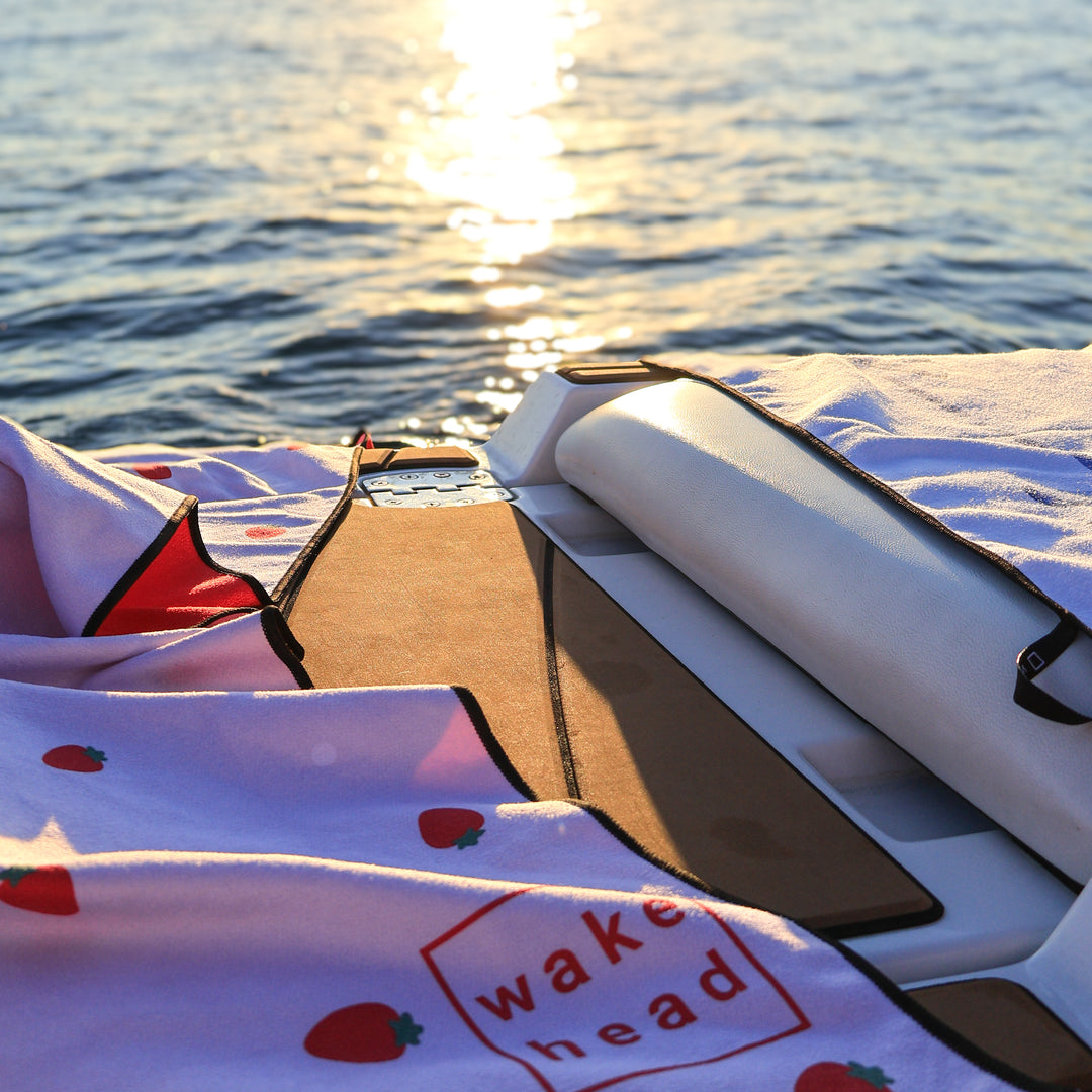 Wake Head Berry Sweet Lake Towel on boat with water and sunset reflection in the background.