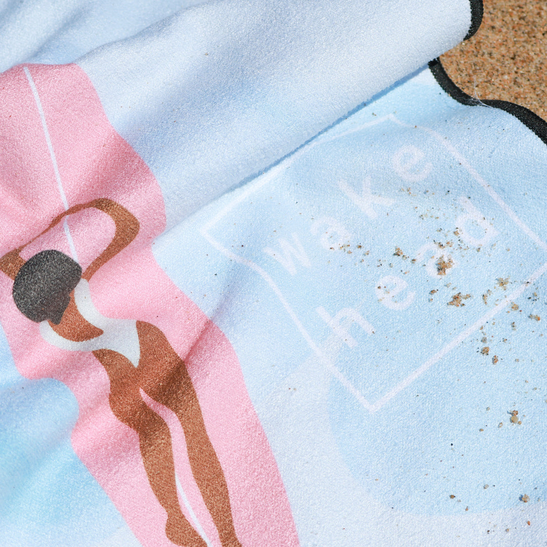 Close-up of a Tide Chaser Lake Towel featuring a colorful design, partially covered with sand on a beach.