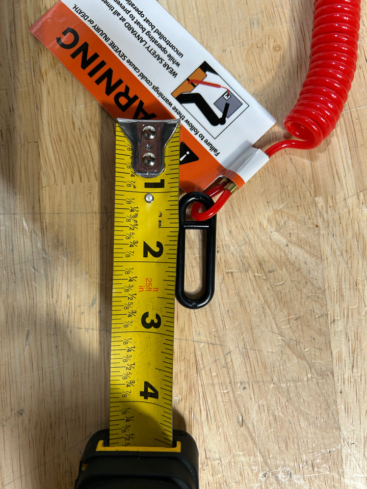 Kill switch lanyard with a red coiled cord and a clip, resting on a measuring tape for size reference.