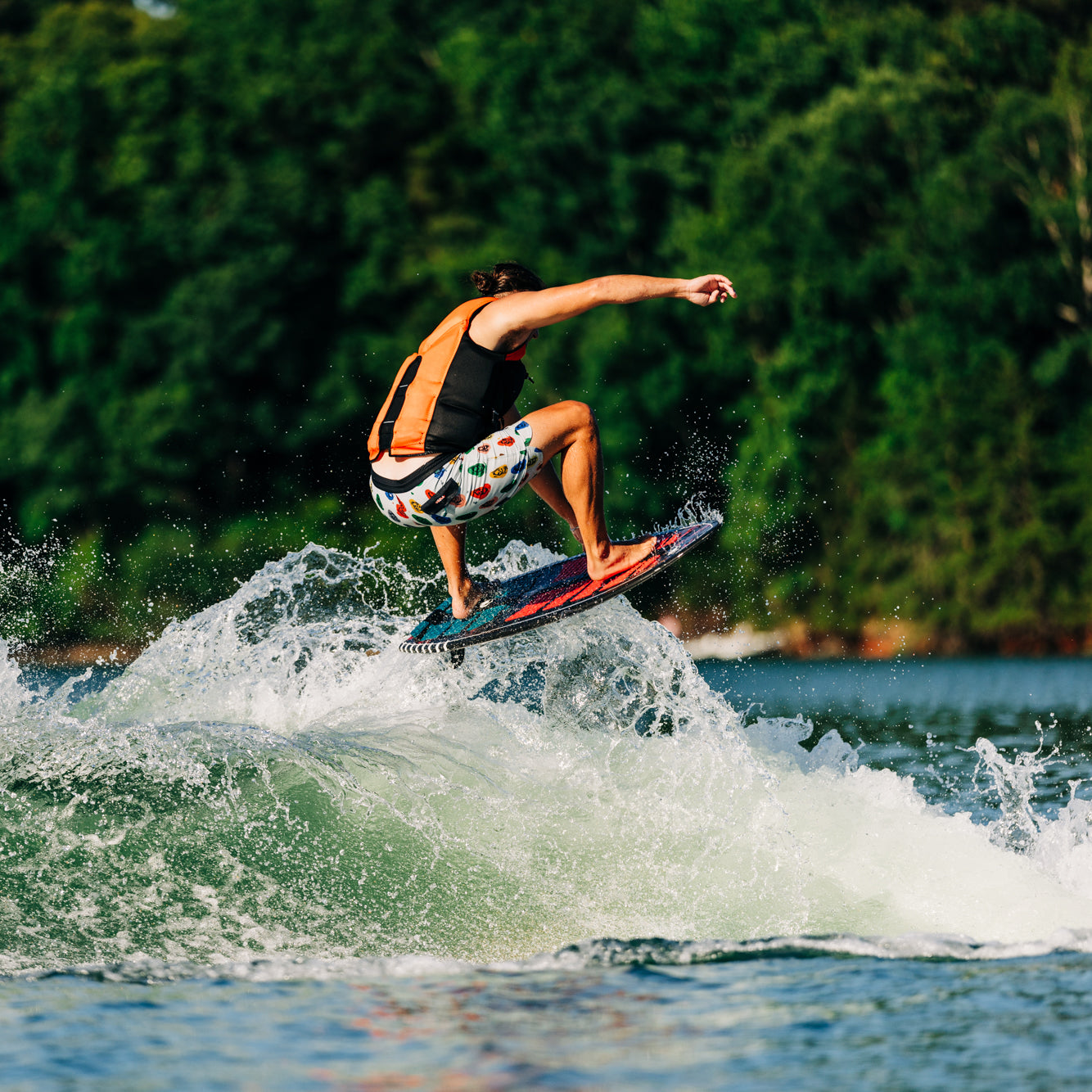 A person performs a jump on the 2025 Liquid Force Syncro Skim Wakesurf Board over a wave on a lake.