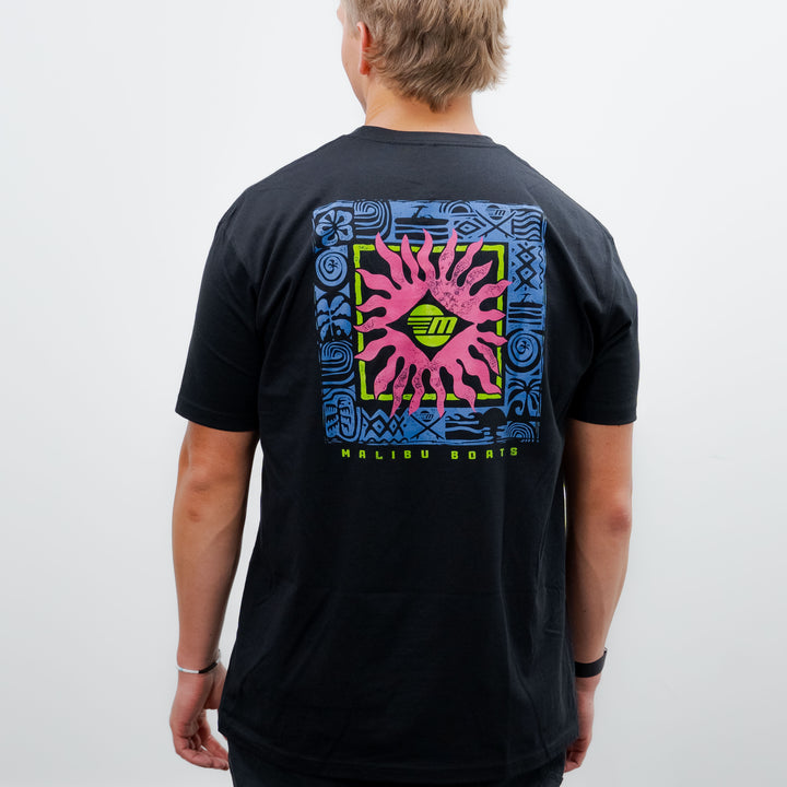 Back view of a person wearing a black Malibu Tribal Tee with colorful tribal-inspired graphic design and "Malibu Boats" text.