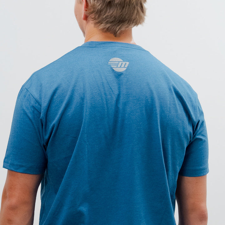 Back view of a person wearing a blue Malibu Icon Tee with a small circular logo on the upper back.