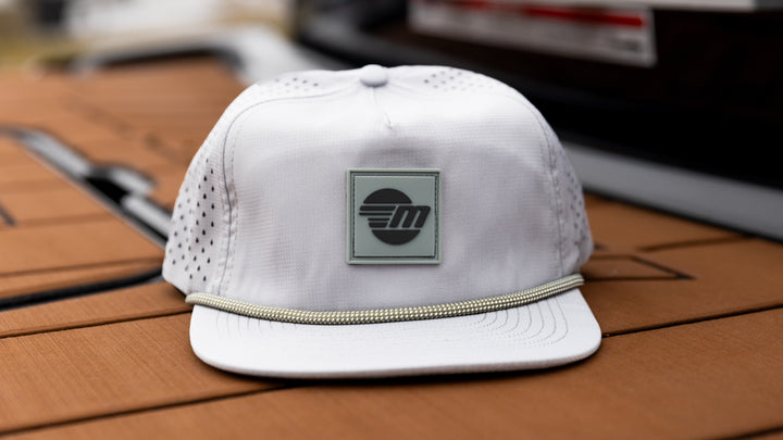White Malibu Dockside Hat with a square logo patch and a decorative rope detail on the brim, placed on a wooden surface.