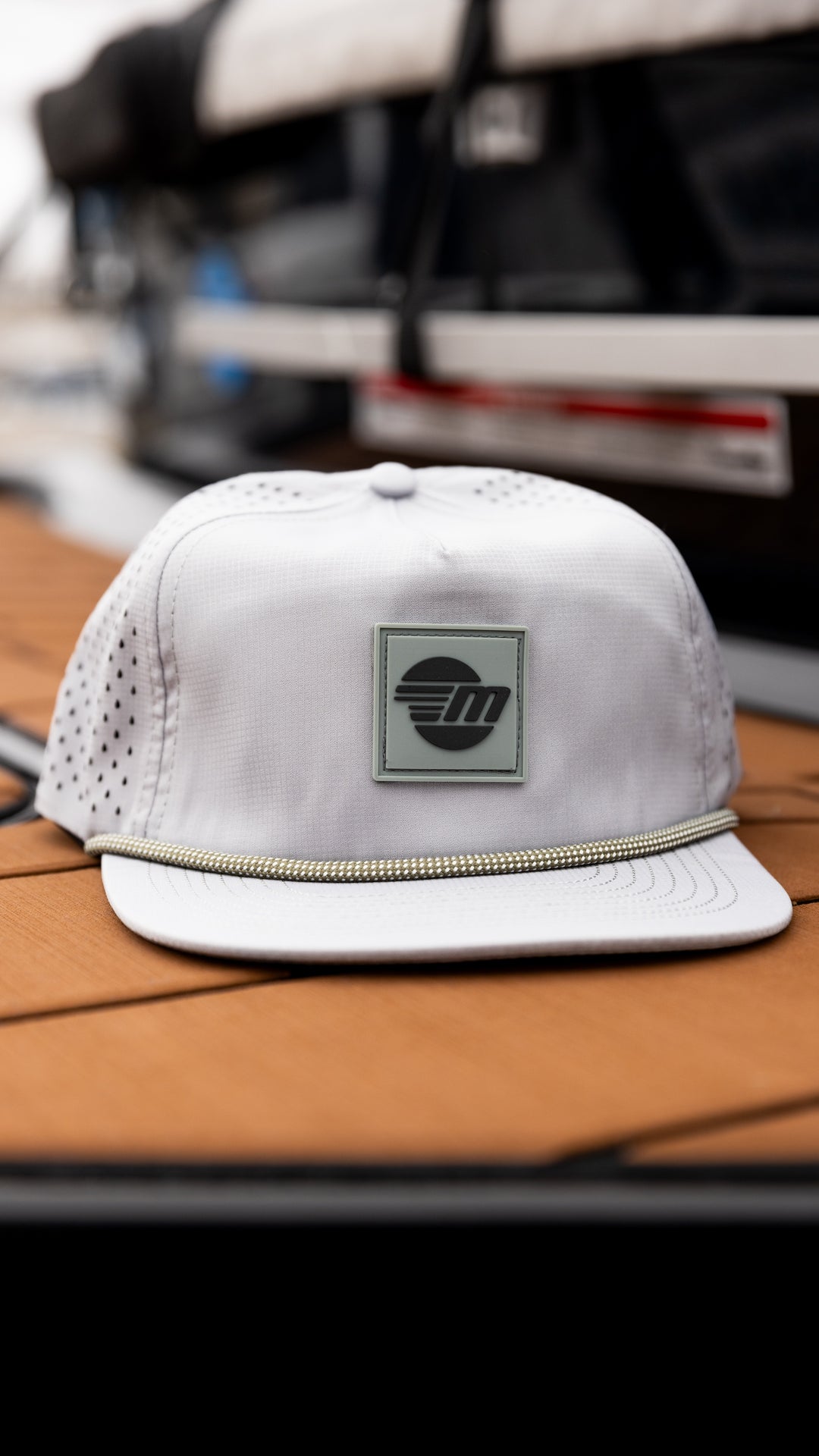 White Malibu Dockside Hat with a logo patch on the front and a decorative rope detail on the brim, placed on a wooden surface.