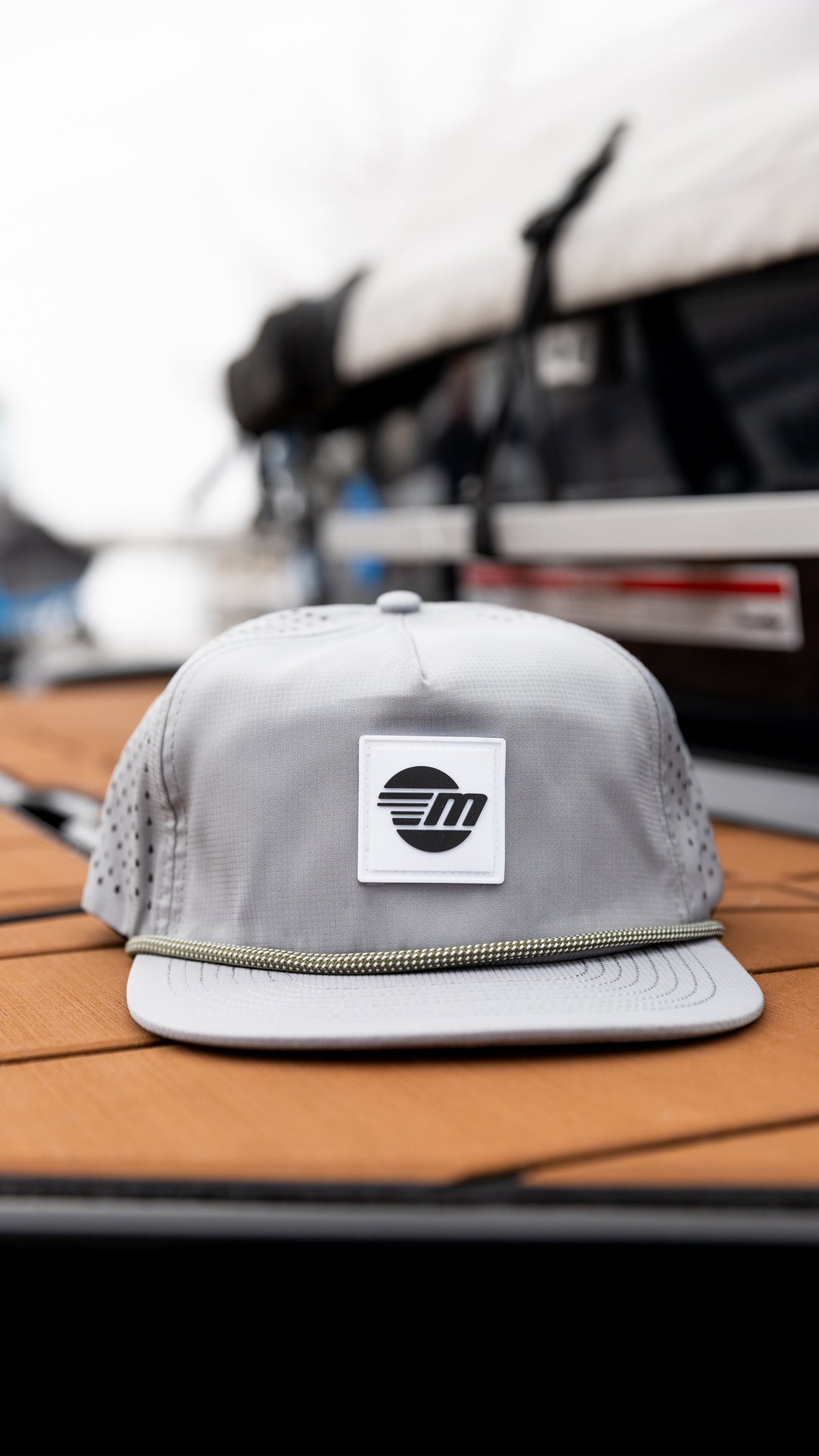 Gray Malibu Dockside Hat with a black and white logo patch, placed on a wooden surface outdoors.