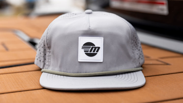 A gray Malibu Dockside Hat with a black and white logo patch on the front, featuring a sun and stylized "M" design.