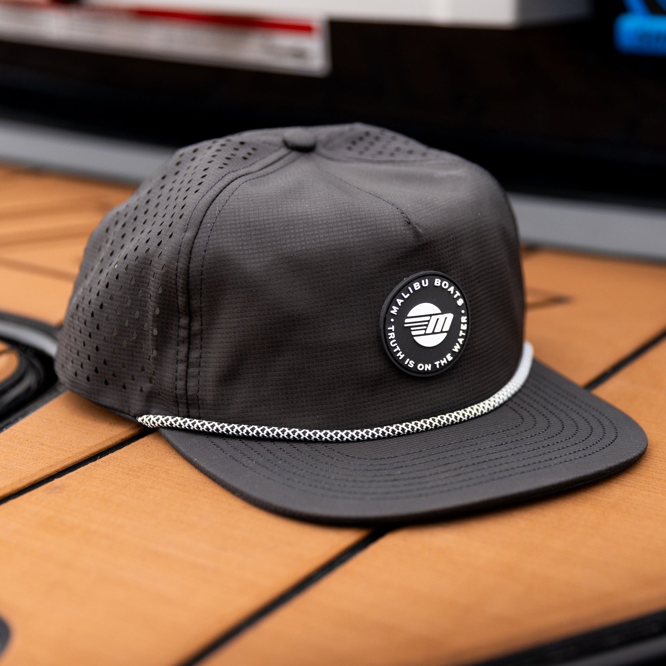 Black Malibu Phantom hat with a circular logo, perforated panels, and a curved brim, placed on a wooden surface.
