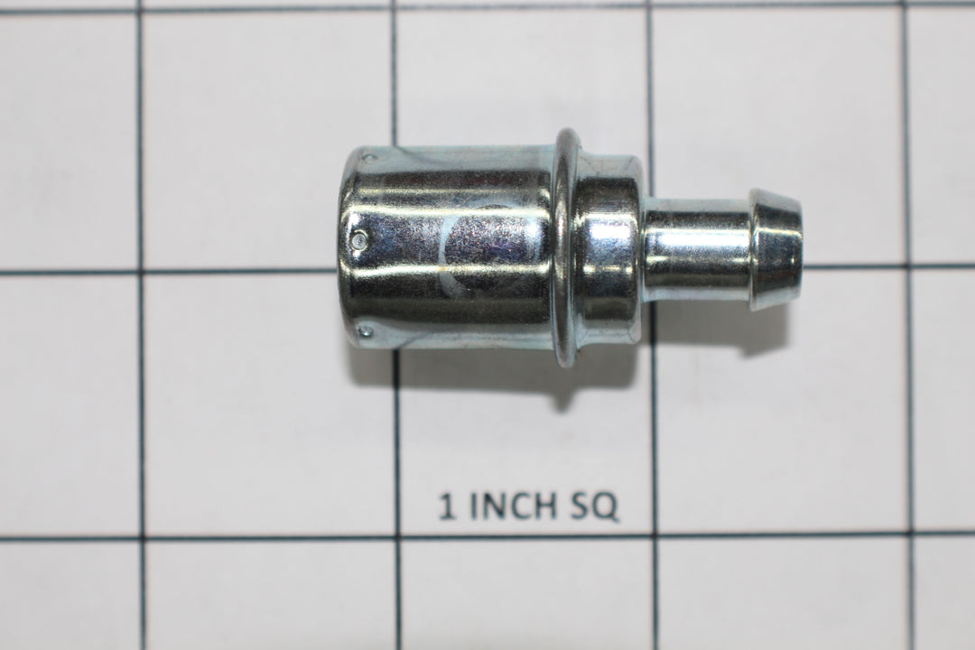 Metal PCV valve lying on a grid with "1 INCH SQ" marking, used to control crankcase pressure in automotive engines.