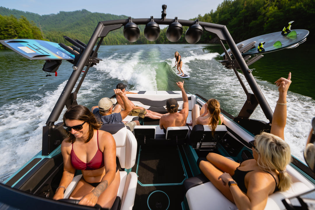 Axis AW20 Tower in black, featuring riders enjoying water sports behind the boat, with a scenic lake backdrop.