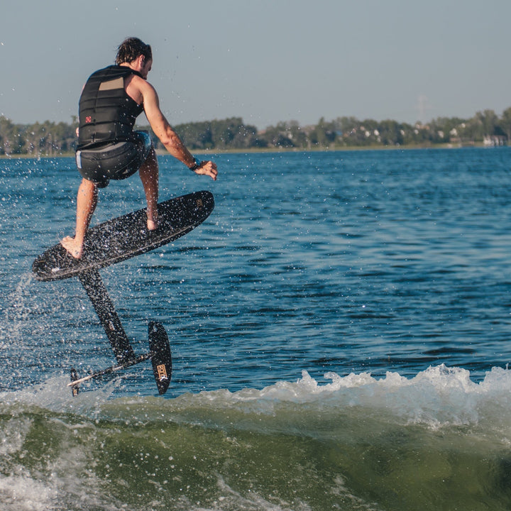 A person riding a high aspect foil board, jumping over a wave on a sunny day, showcasing the Expert 29" Velo with Blackbird design.