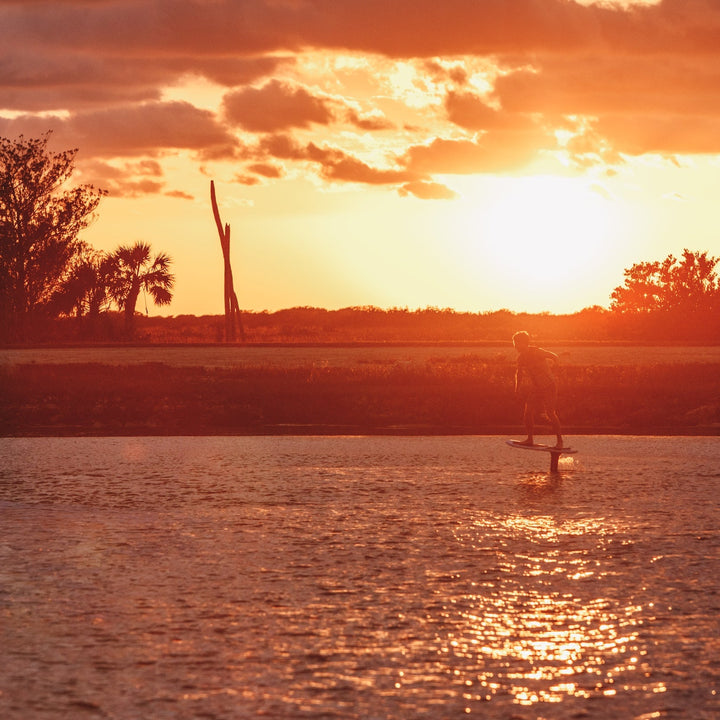 A person riding a high aspect foil board at sunset, reflecting vibrant colors on the water&