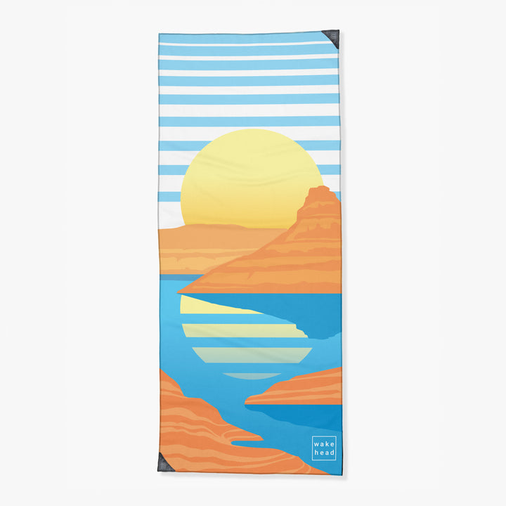 Colorful tower towel featuring a sunset over desert cliffs and a blue river, with "wake head" branding in the corner.