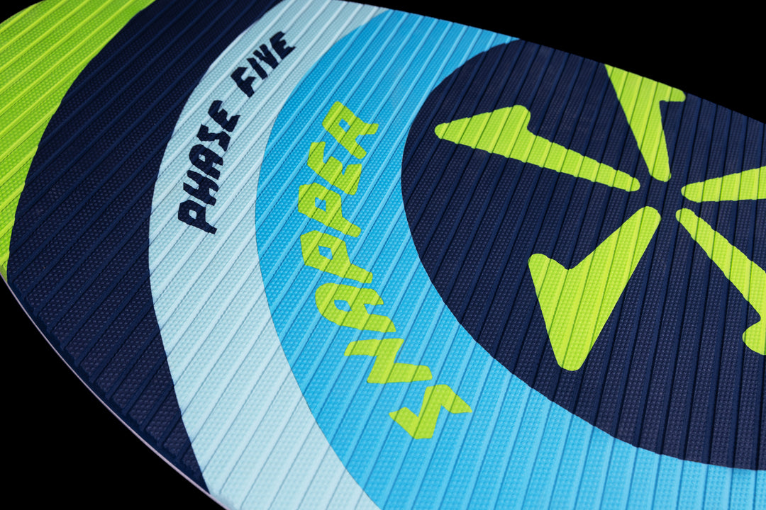 Close-up of the 2025 Phase 5 Snapper Skim Board featuring a blue, white, and neon yellow design with textured surface and bold branding.