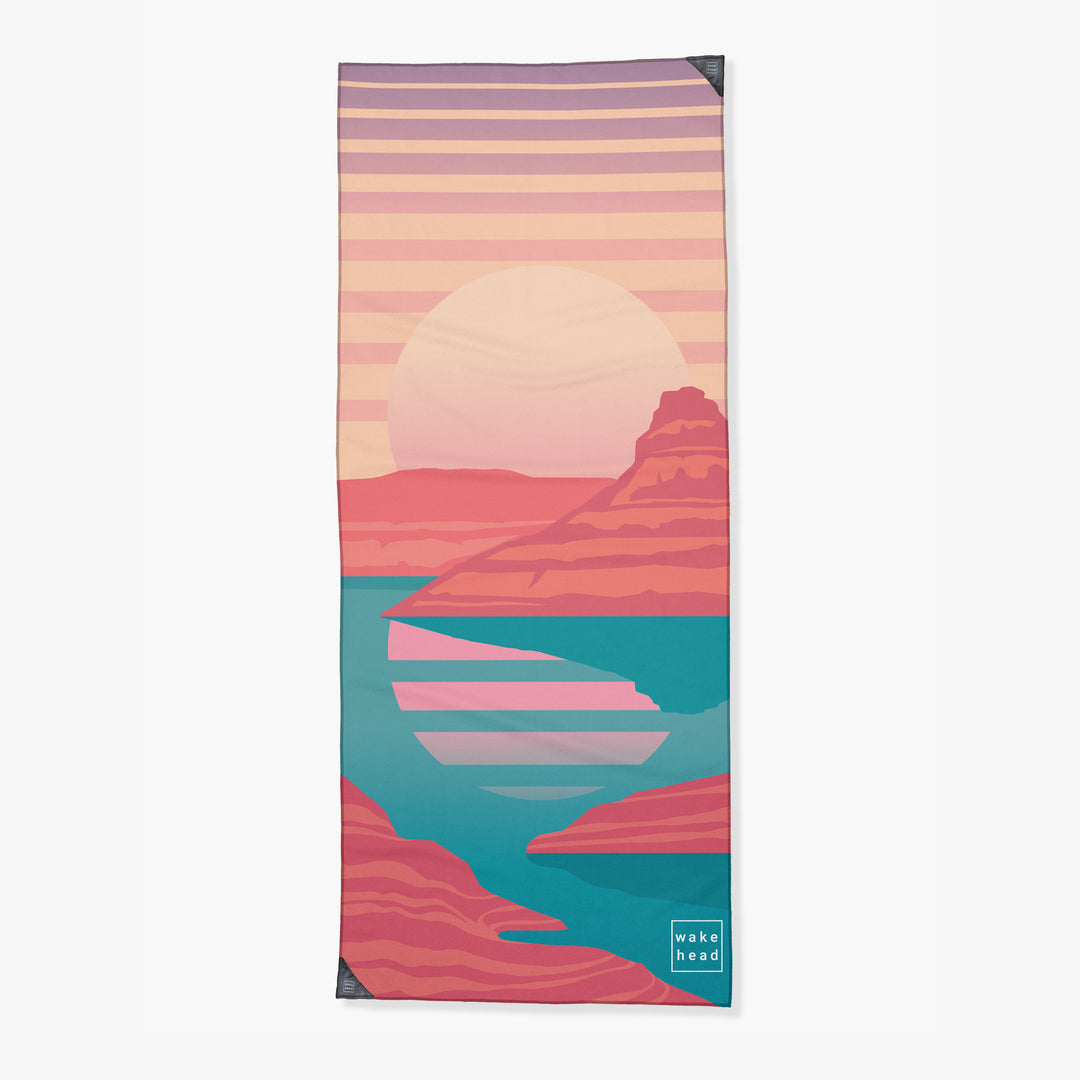 Colorful tower towel featuring a sunset over mountains and water, with a "wake head" logo in the bottom corner.