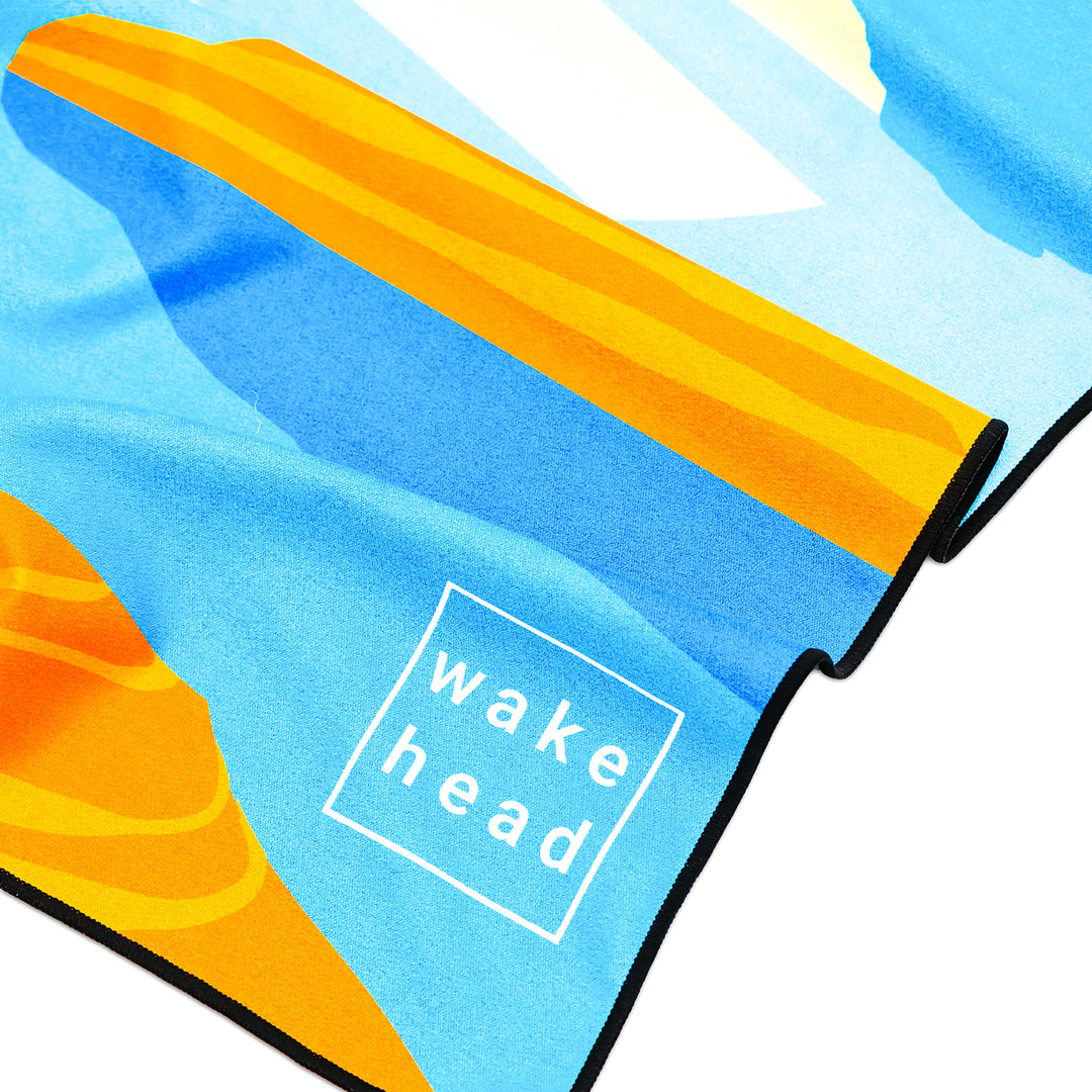 Colorful Powell Towel featuring a beach scene with a yellow surfboard and "wake head" text in a white box.