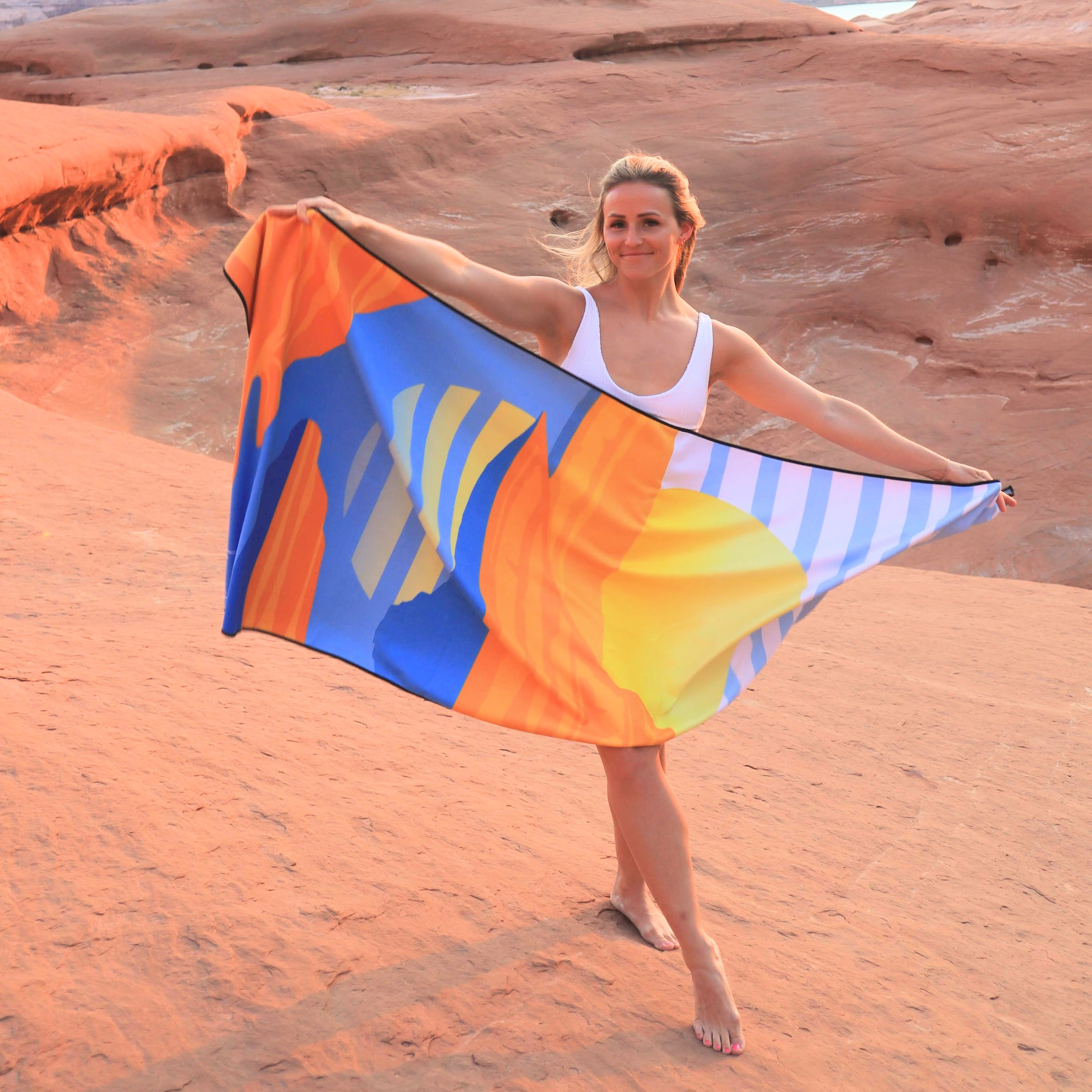 Woman holding a colorful Powell Towel with a sunset background, showcasing the vibrant, abstract design and soft fabric.