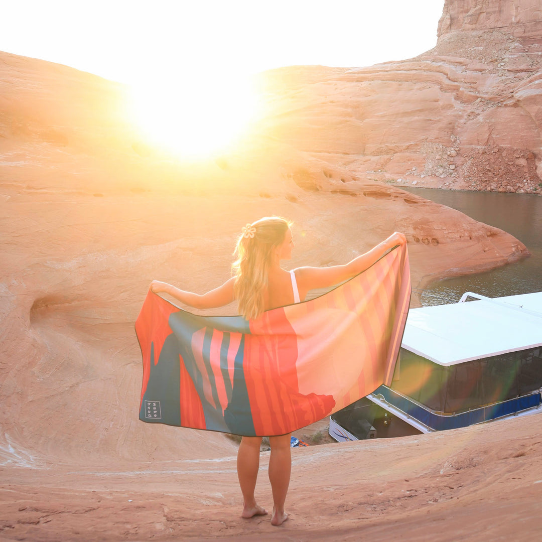 Woman holding a Powell Towel at sunset near a desert canyon with water, showcasing the product&