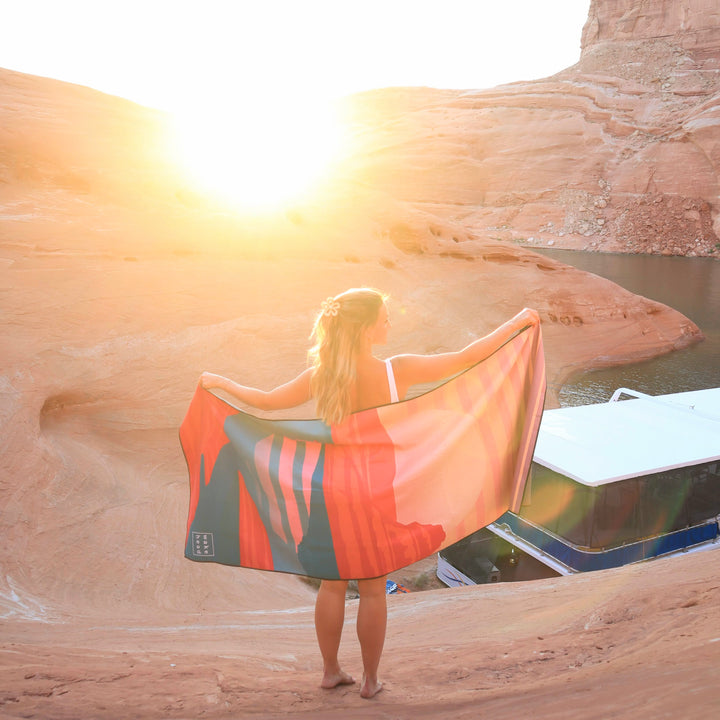 Woman holding a Powell Towel at sunset near a desert canyon with water, showcasing the product&
