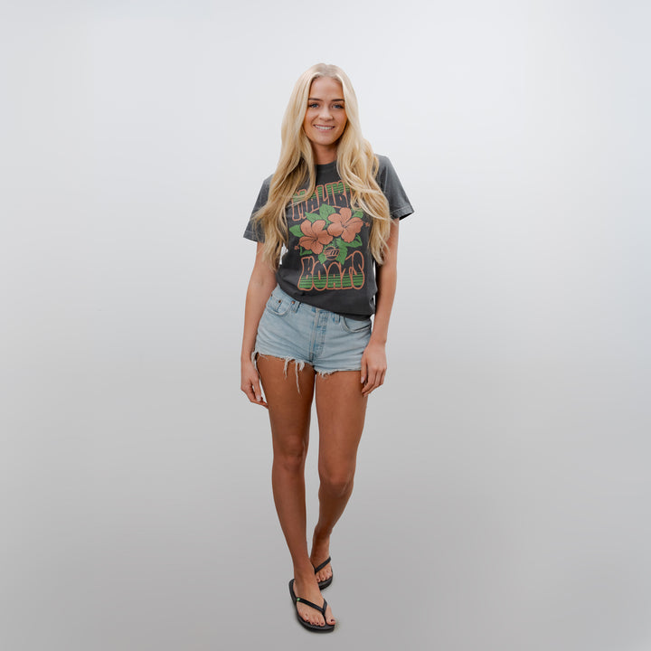 Model wearing a Malibu Aloha Tee with floral graphics, paired with denim shorts and flip-flops, showcasing a casual summer look.