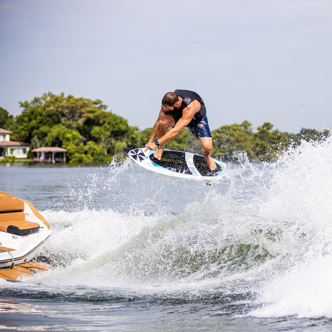 A man performs a jump on a 2026 Phase Five Ahi surfboard while riding a wave behind a boat.