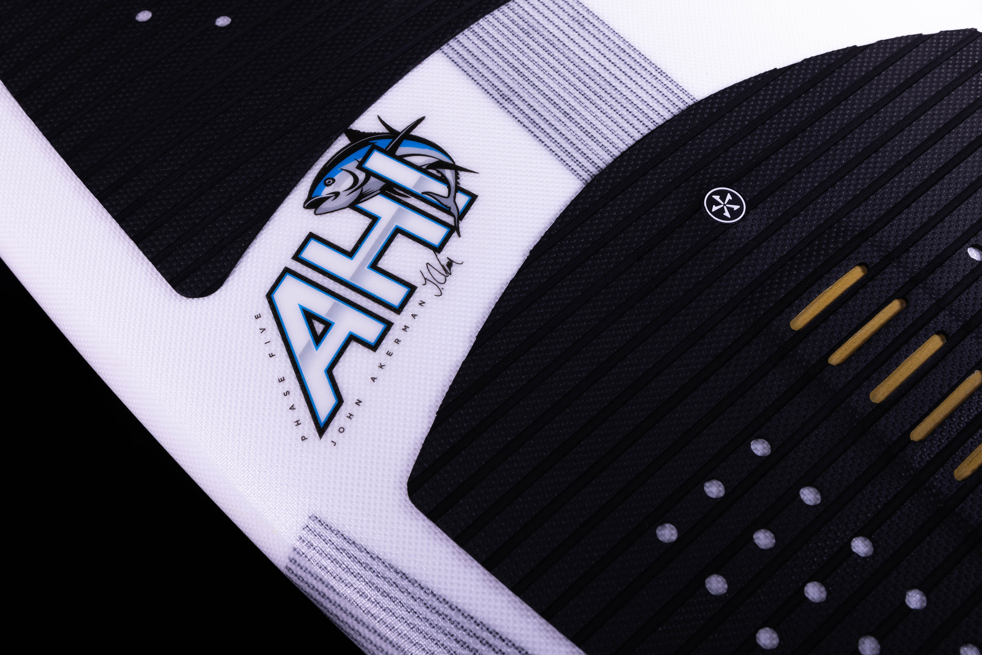 Close-up of the 2025 Phase 5 Ahi surfboard featuring a black and white design with yellow accents and a John Akerman signature.