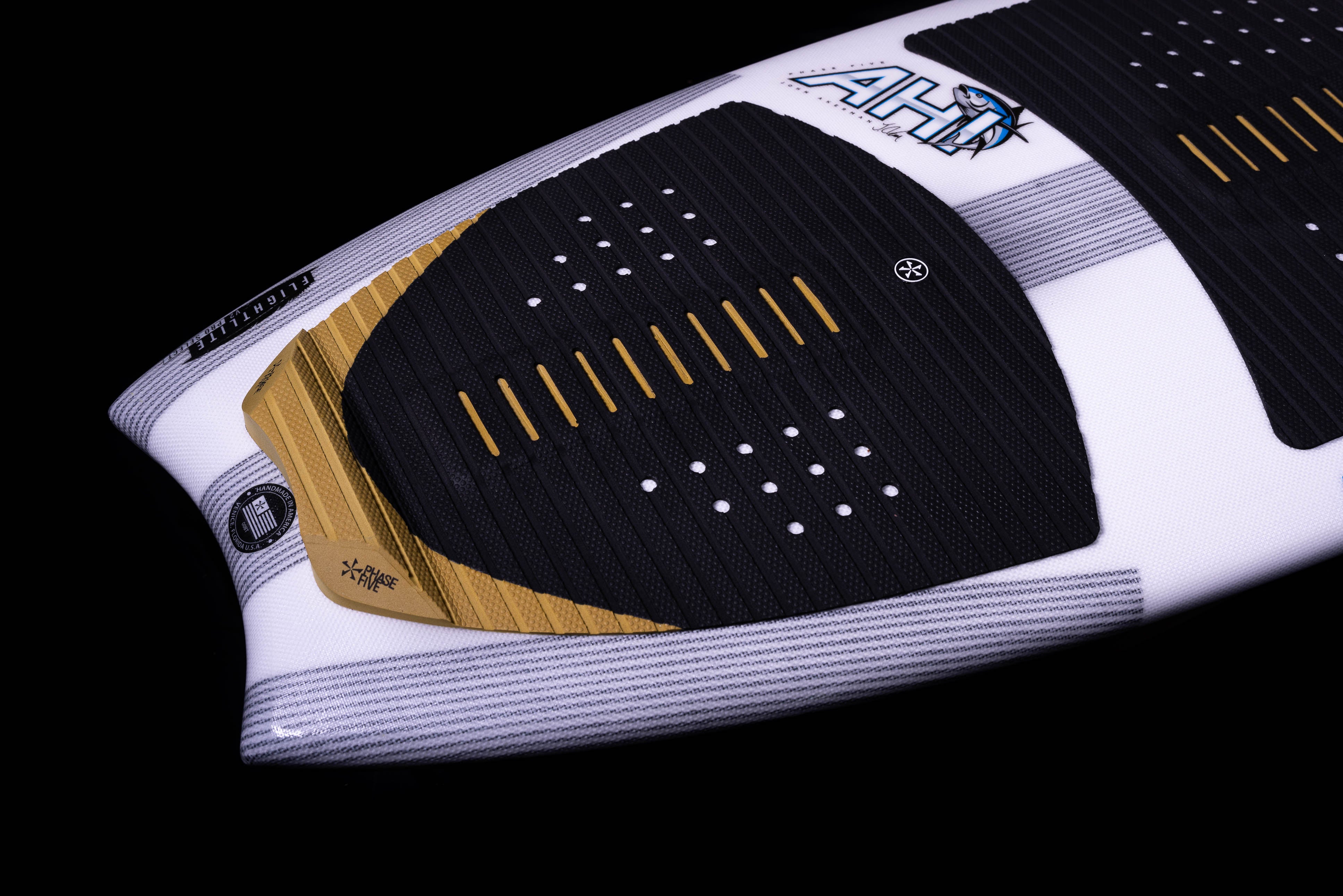 Close-up of the 2025 Phase 5 Ahi surfboard featuring a white, black, and gold design with textured grip pads and branding details.