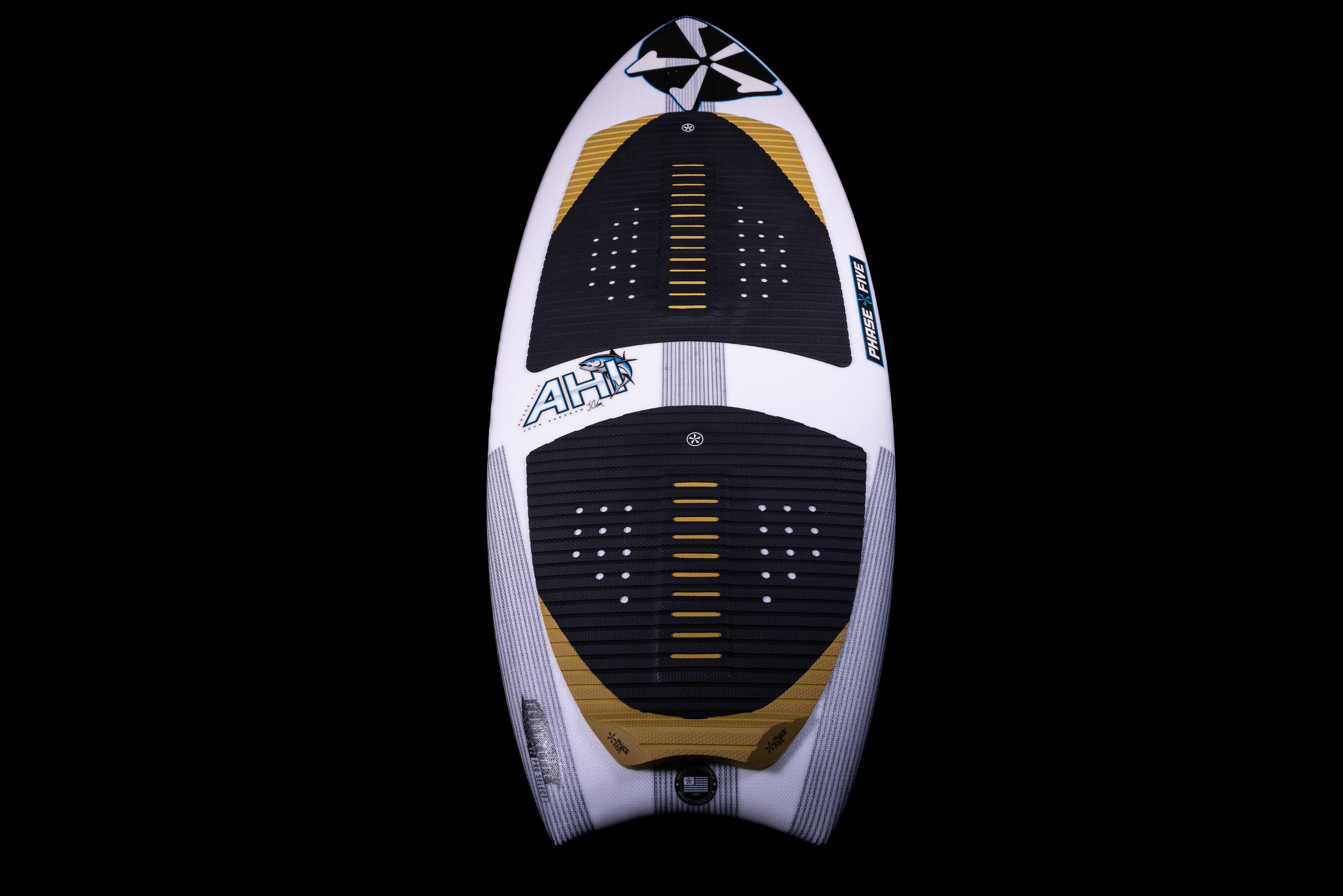 2025 Phase 5 Ahi surfboard with black, white, and gold design, featuring traction pads and a fin, on a black background.