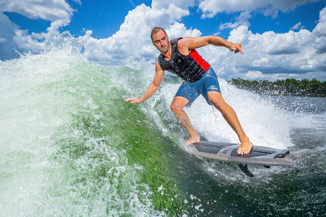 A male surfer riding a wave on the 2025 Phase 5 Ahi Stealth Surfboard outdoors under a partly cloudy sky.
