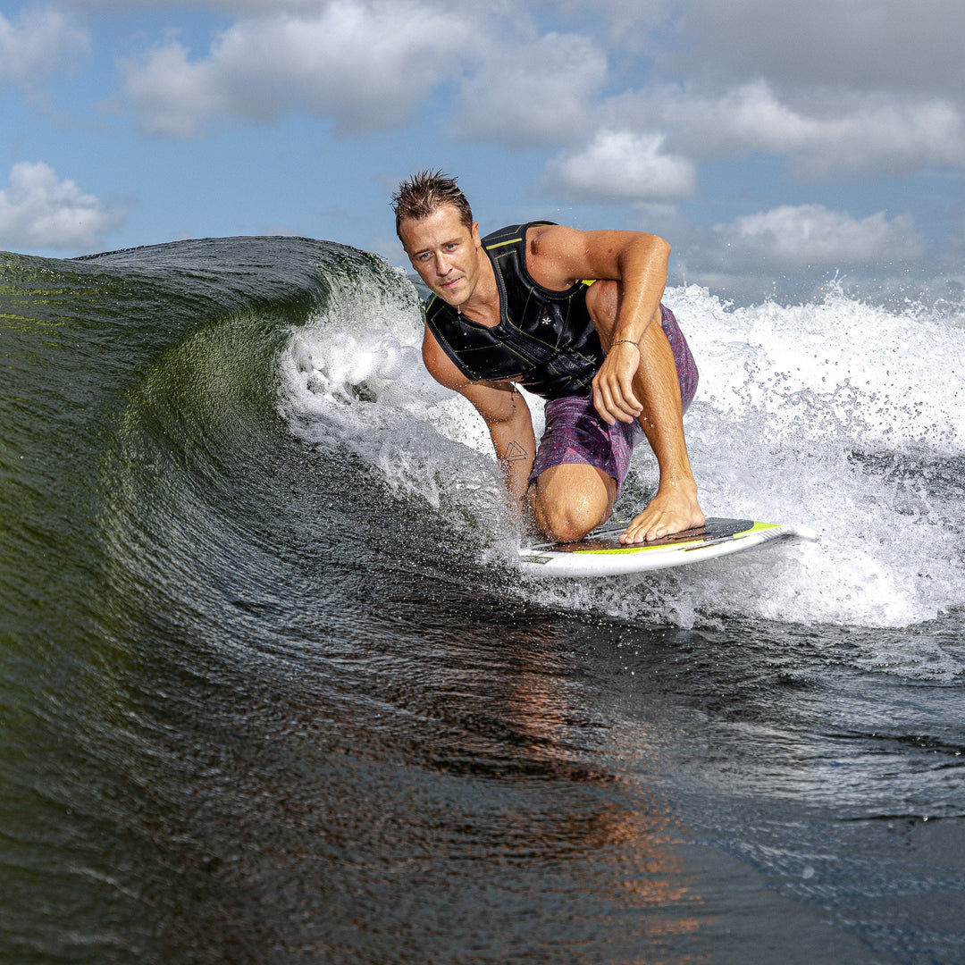 A surfer skillfully rides a wave on a Phase Five Aku V2 board, showcasing dynamic movement and water spray.