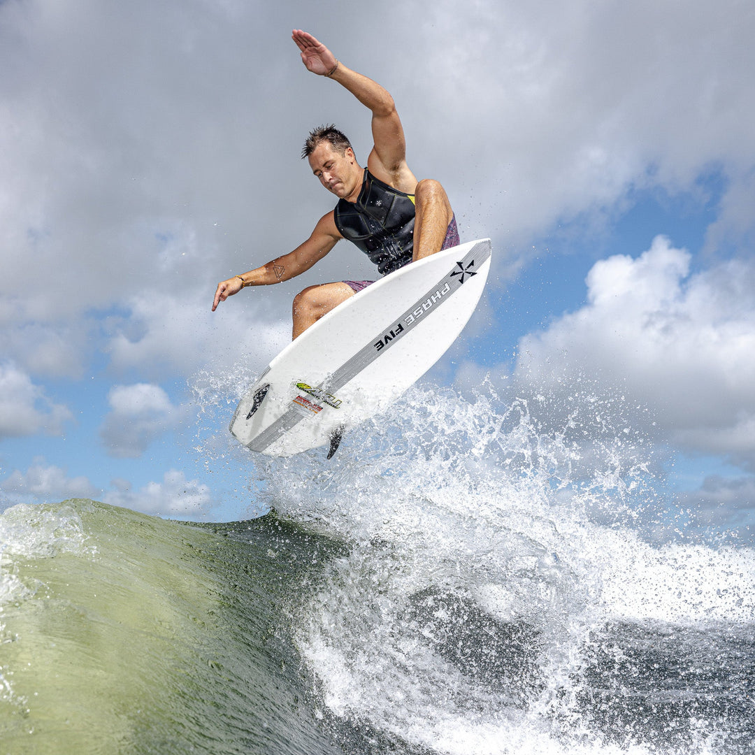 A surfer performs a jump on a 2026 Phase Five Aku V2 board above a wave, showcasing dynamic movement and skill.