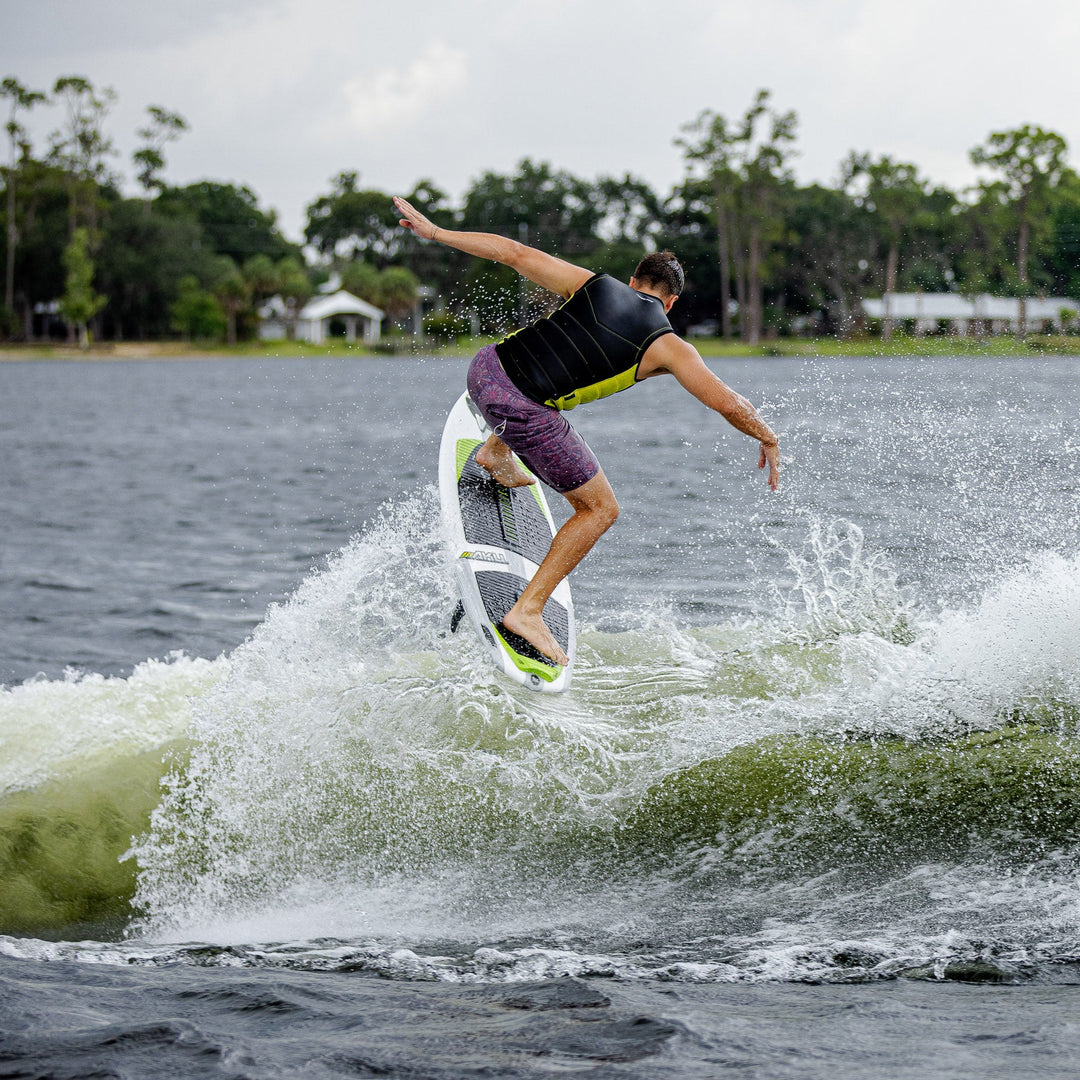 A person performing a trick on the 2026 Phase Five Aku V2 surfboard, creating a spray of water behind them.