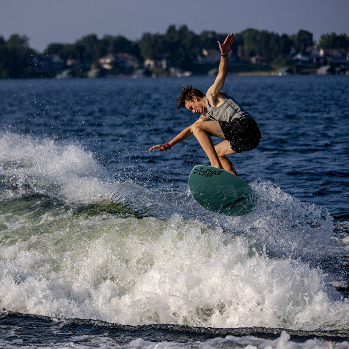 A rider performs a jump on the 2026 Phase Five Avenger surfboard, creating a splash in the water.