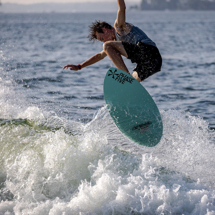 A rider performs a jump on the 2026 Phase Five Avenger surfboard, creating a splash in the water.